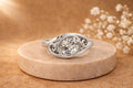 2 CT oval cut lab grown diamond bypass bezel ring displayed on a stone pedestal with soft warm lighting.