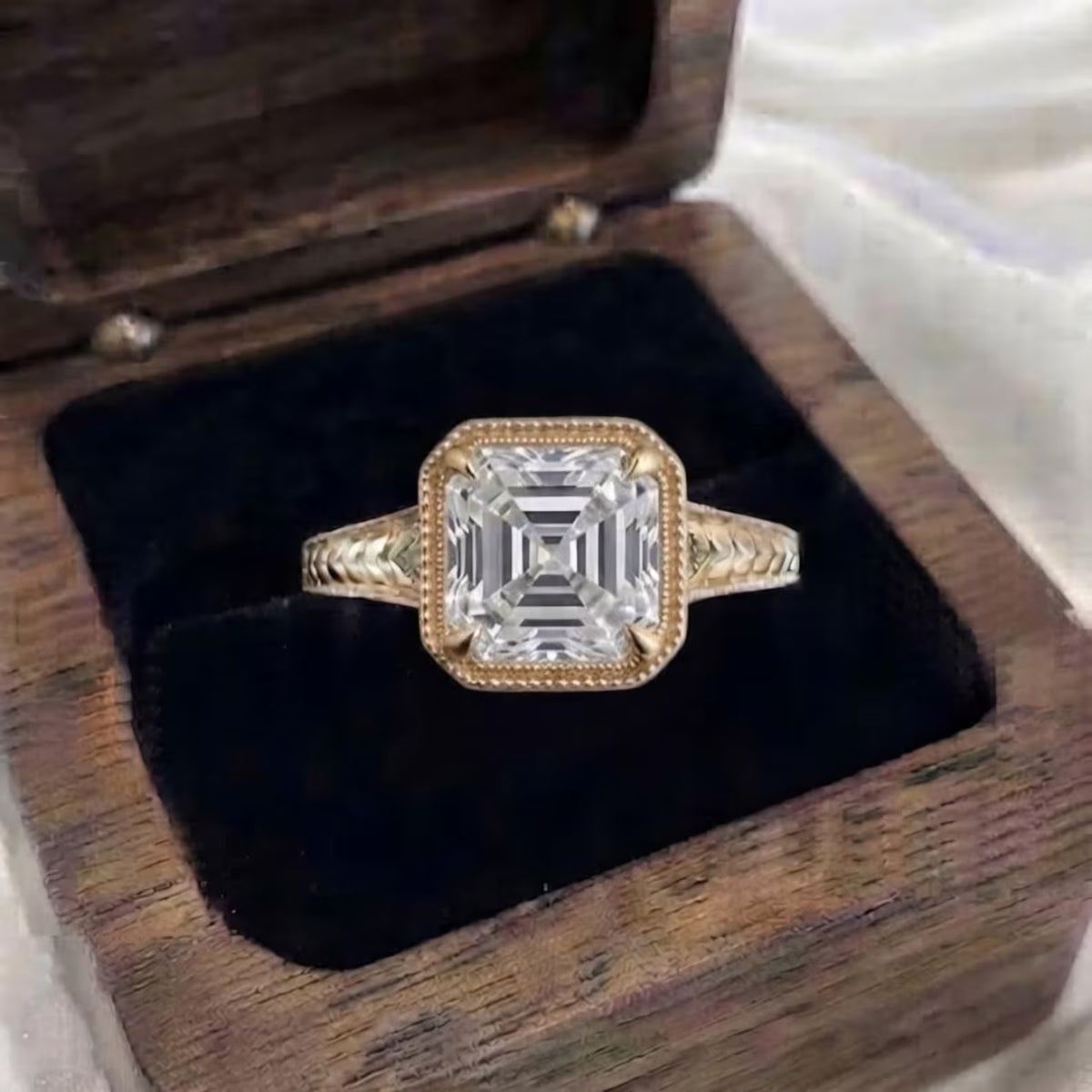 Top view of 3 CT Asscher cut lab grown diamond yellow gold ring in wooden box with milgrain bezel setting
