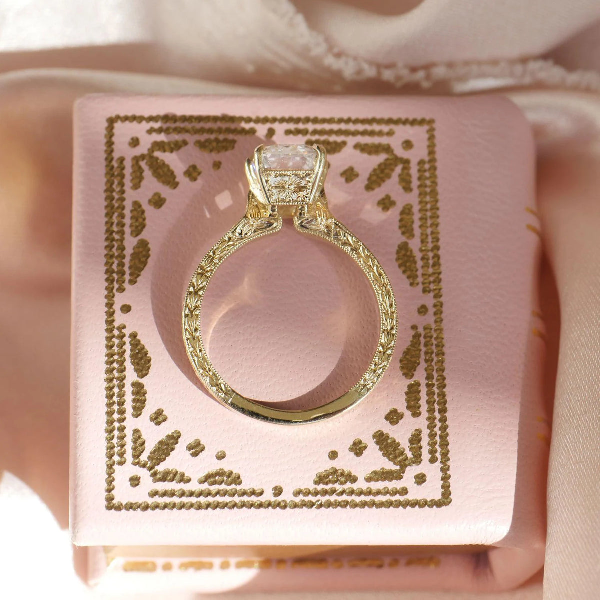 Profile view of yellow gold vintage Asscher diamond solitaire ring resting on a pink jewelry box