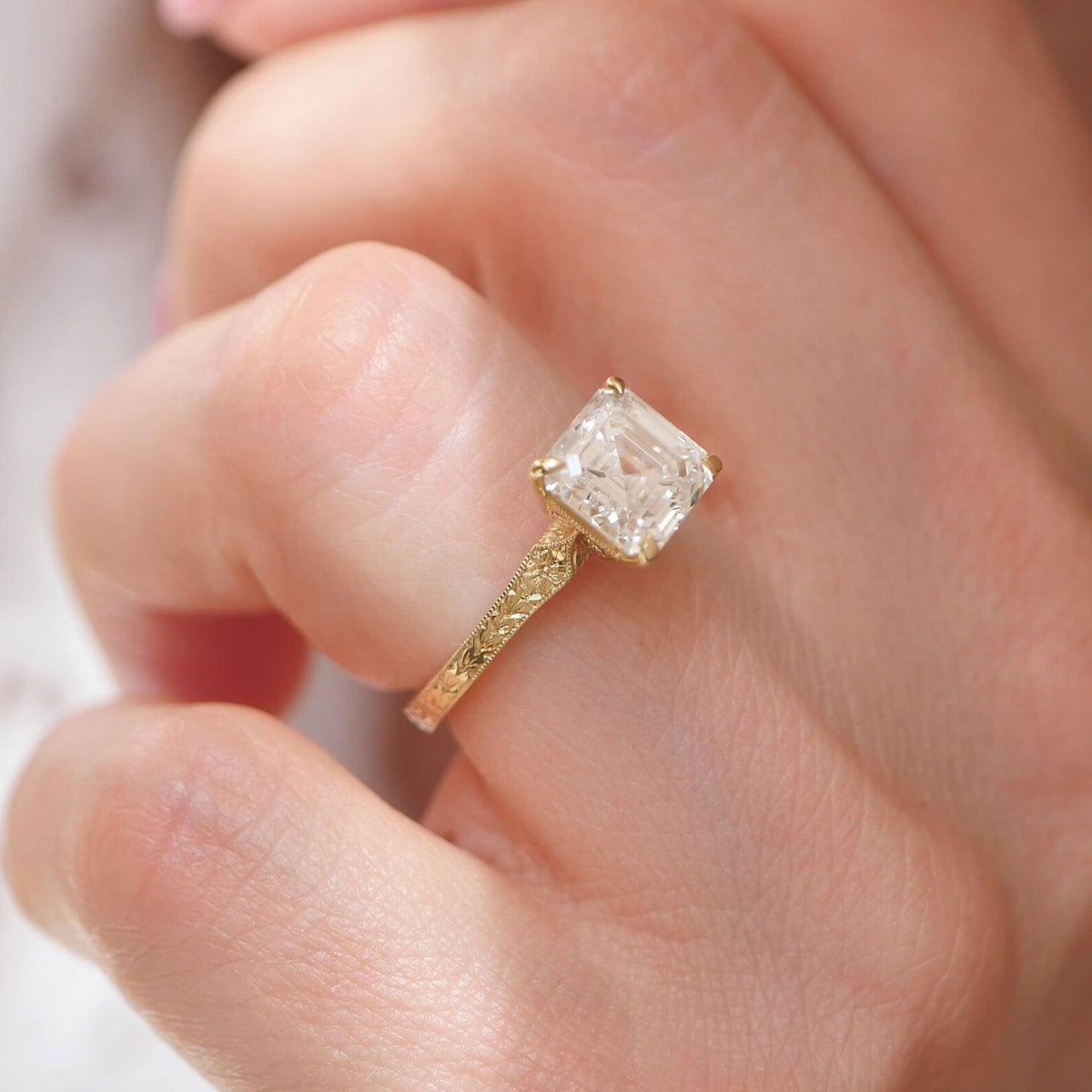 Top-down view of 2 carat Asscher lab diamond ring showing botanical leaf carved shank against pink background