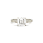 An emerald-cut diamond engagement ring with a silver-toned band featuring delicate filigree detailing on the shoulders, set against a plain white background.