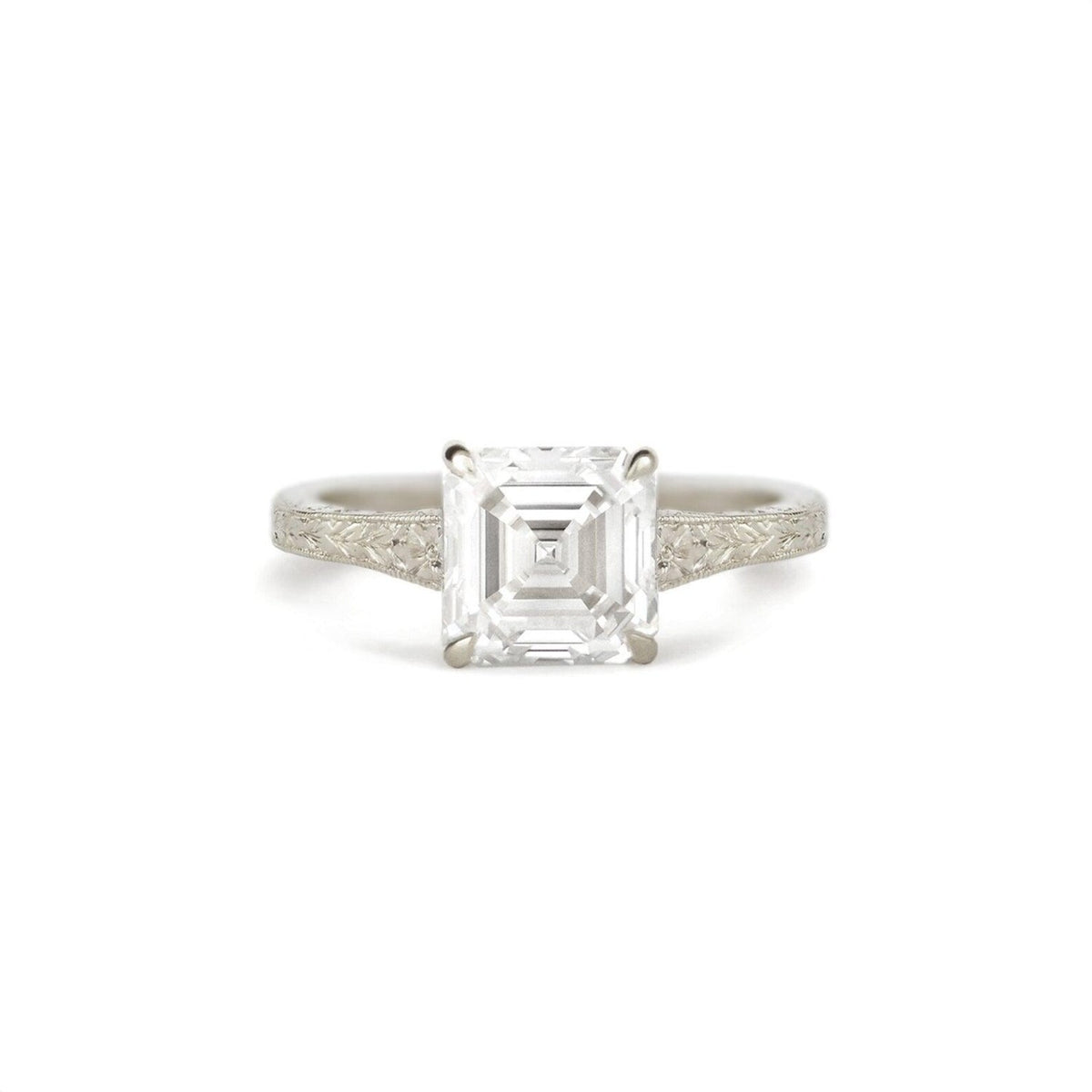 An emerald-cut diamond engagement ring with a silver-toned band featuring delicate filigree detailing on the shoulders, set against a plain white background.