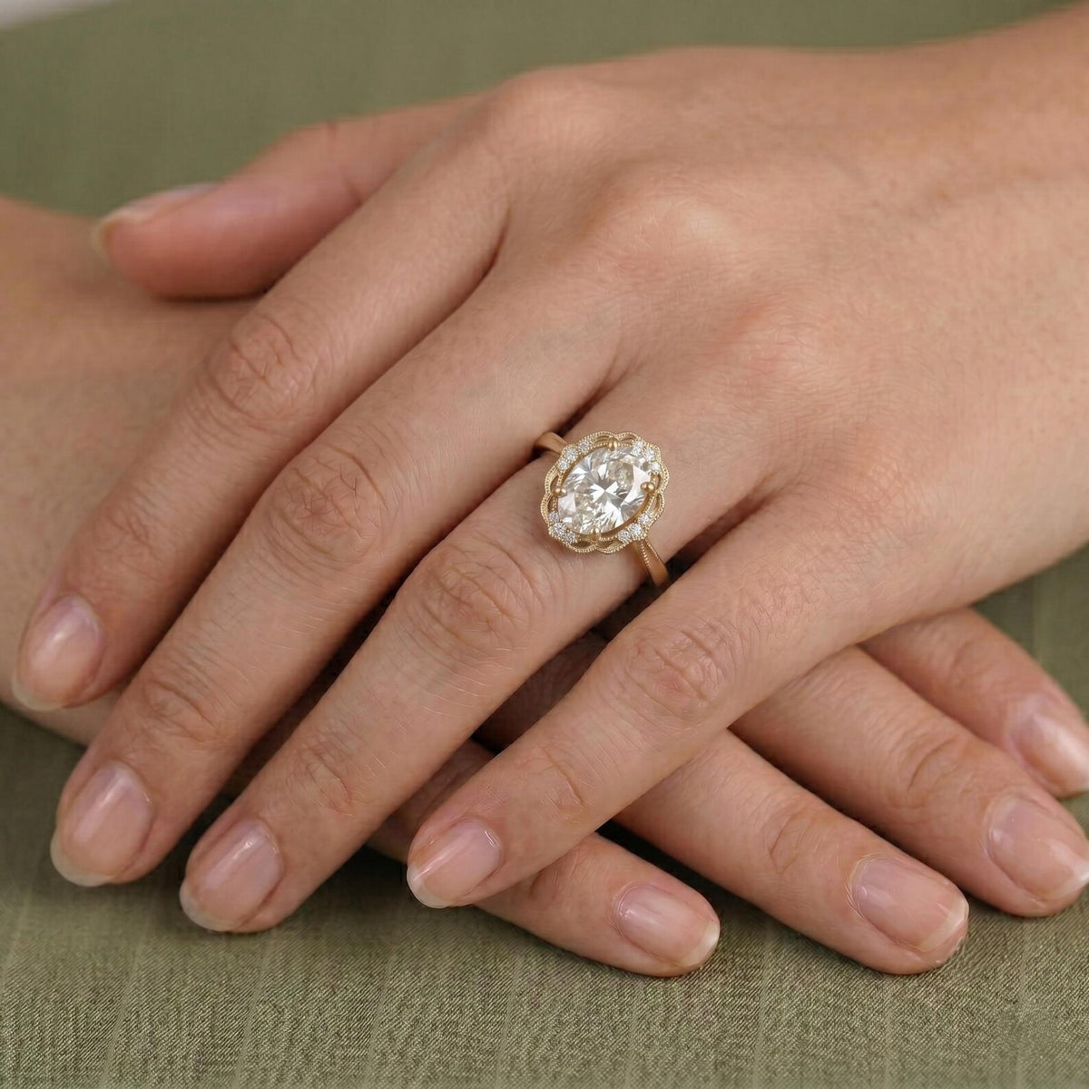 On-hand view of a 3 carat oval lab grown diamond engagement ring with a vintage scalloped diamond halo in yellow gold.