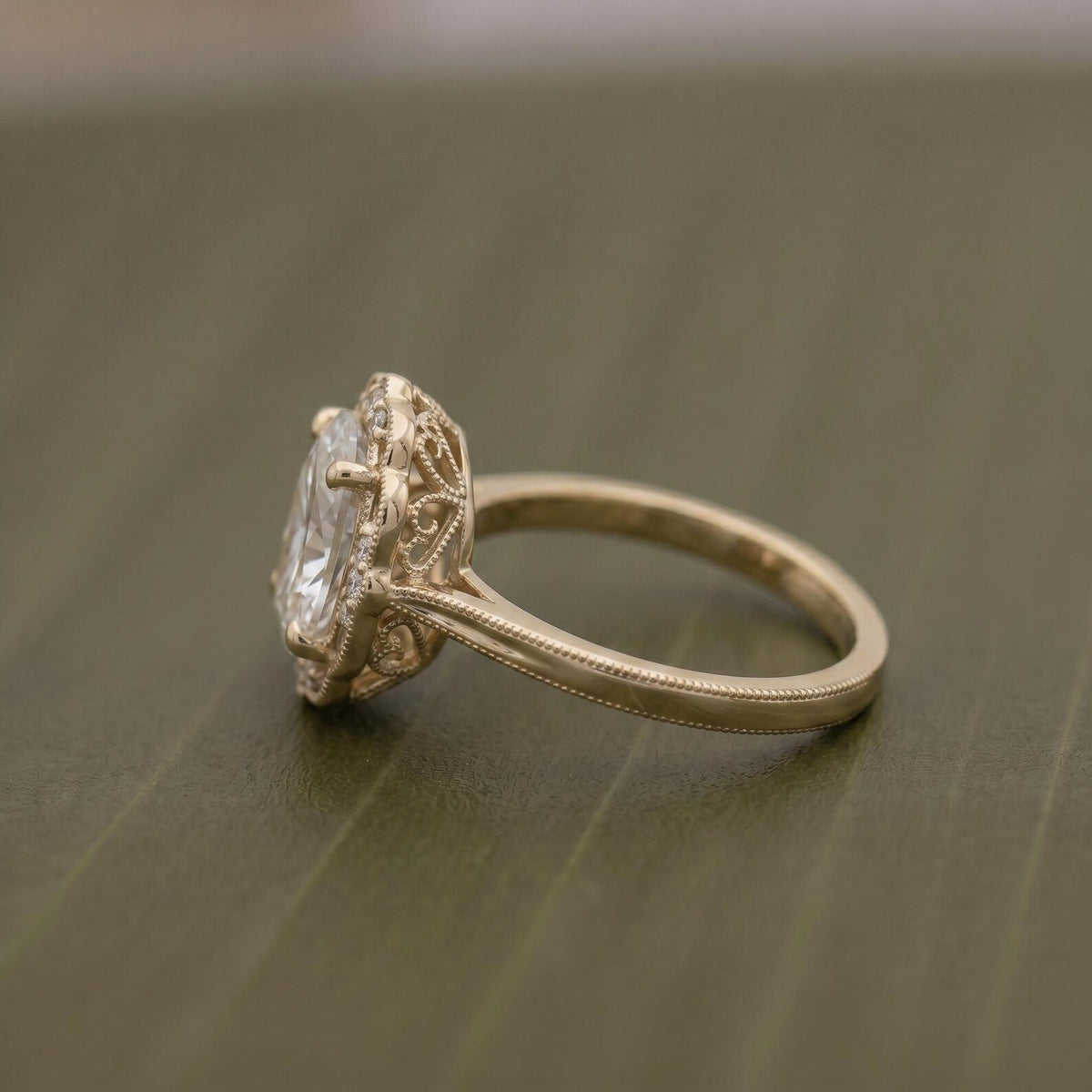 Close-up side perspective of a yellow gold vintage engagement ring featuring a 3 CT oval center diamond and decorative openwork gallery.