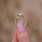 Side profile view of a 3 carat oval lab grown diamond ring in yellow gold held between fingers, featuring a milgrain detailed bezel basket.
