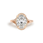 Studio display of a 3 carat oval lab created diamond ring set in 14k rose gold featuring a vintage milgrain border bezel setting.