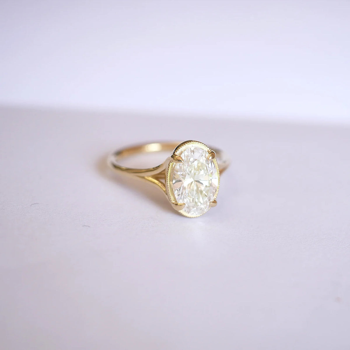 Three-quarter perspective angle view of a 3ct oval lab grown diamond solitaire ring with split cathedral shoulders resting on a smooth white surface.