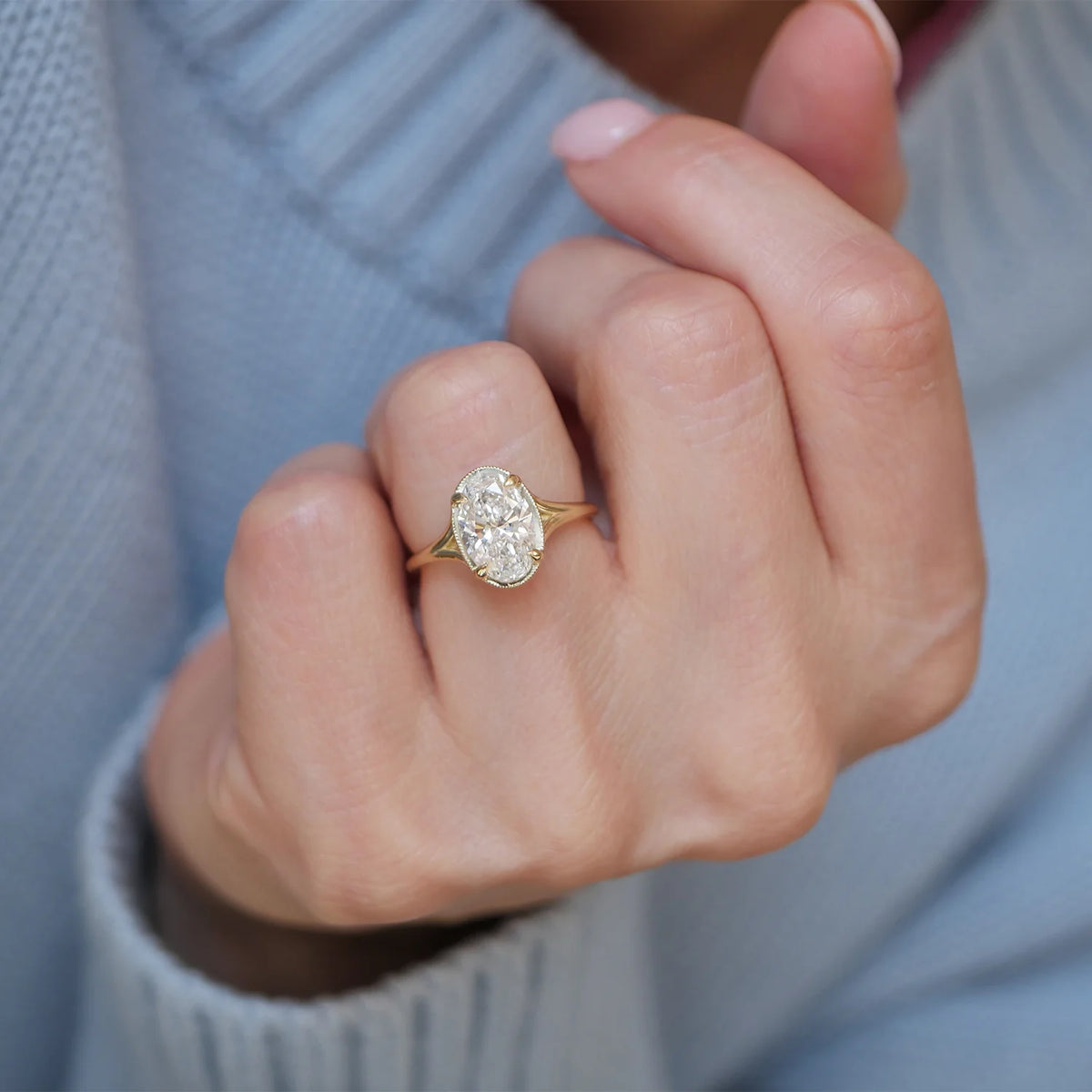 Elegant lifestyle photo of a 3 carat oval lab grown diamond ring with split shoulders showcased on a ring finger.