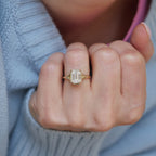 Top-down lifestyle shot of a 3 carat emerald cut lab diamond ring worn on a finger against a light blue knitted sweater.