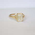 Three-quarter angled studio shot of a 3 CT emerald cut lab diamond ring with split shoulders resting on a white surface.