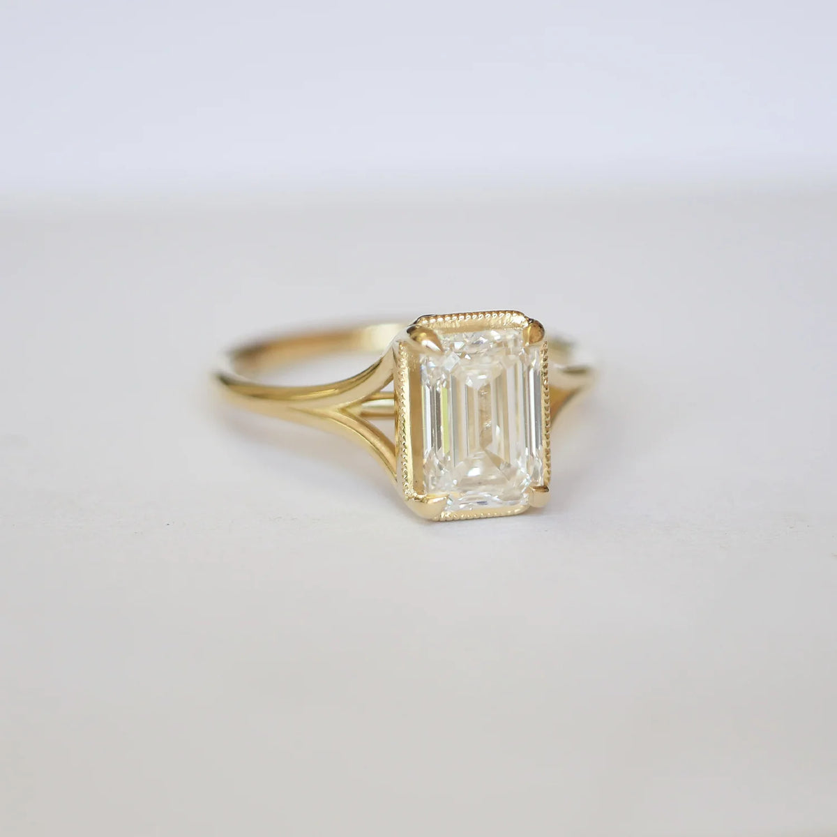 Three-quarter angled studio shot of a 3 CT emerald cut lab diamond ring with split shoulders resting on a white surface.