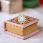 Creative product photography of a 3 carat emerald cut lab diamond Art Deco ring resting on a vintage pink mini book.