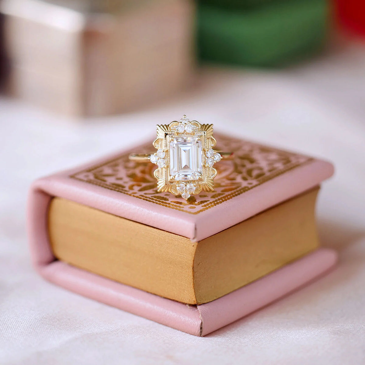 Creative product photography of a 3 carat emerald cut lab diamond Art Deco ring resting on a vintage pink mini book.