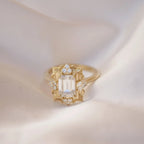Close-up shot of a 3 carat emerald cut lab grown diamond halo ring resting on smooth white satin fabric.