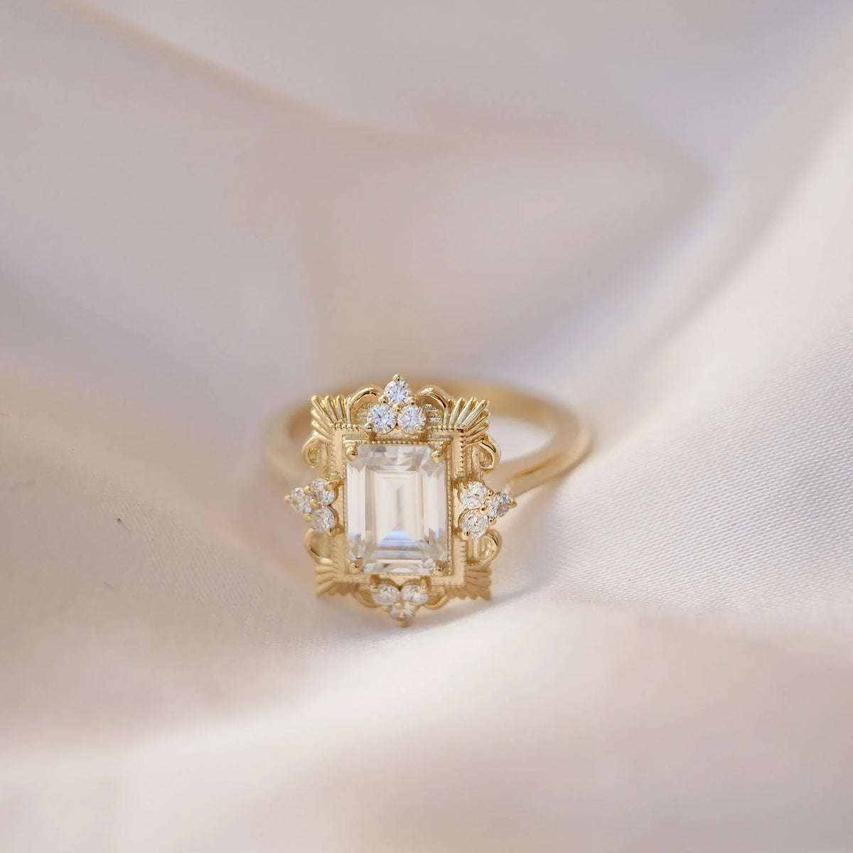 Close-up shot of a 3 carat emerald cut lab grown diamond halo ring resting on smooth white satin fabric.