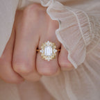 Top-down hand shot of a woman wearing a 3 carat emerald cut lab diamond ornate halo ring against romantic ruffled silk cuff.