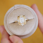 Overhead view of a 3 carat emerald cut lab diamond Art Deco halo ring presented inside a beige velvet round jewelry box.