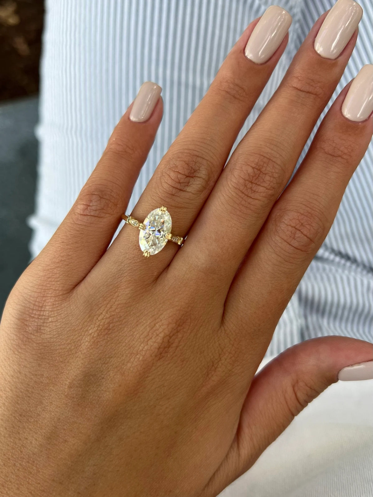 On-hand photo of a woman wearing a 4 CT oval lab grown diamond engagement ring in yellow gold.