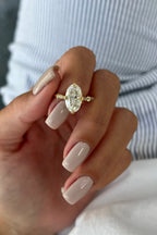 Close up image of hand holding 4 CT oval lab diamond engagement ring displaying vintage shoulder detail.