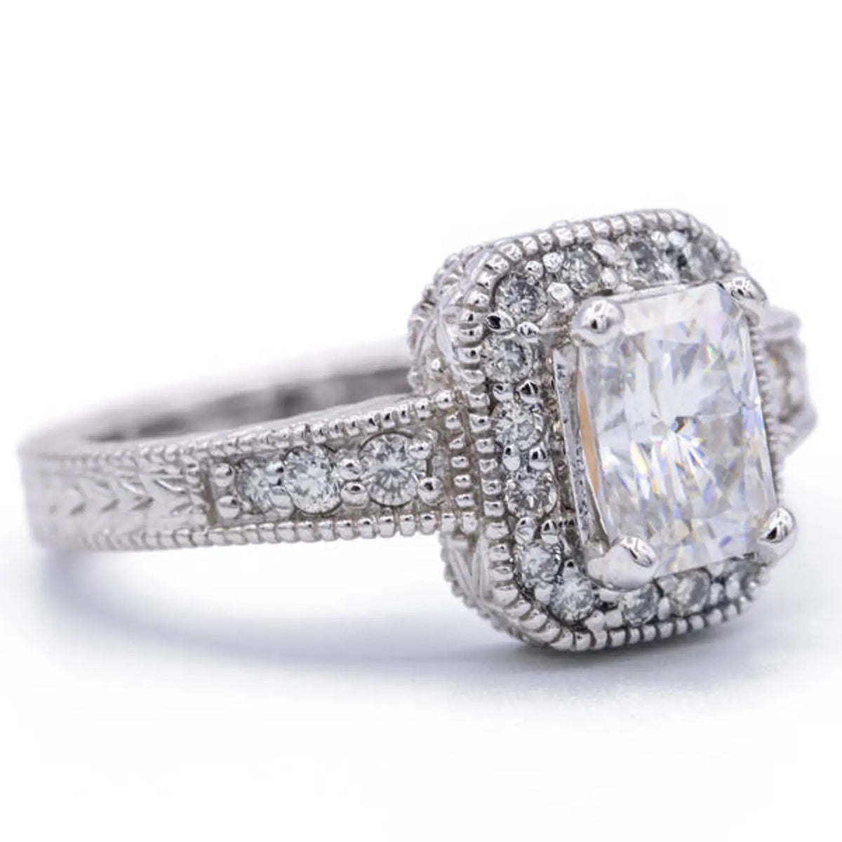 Perspective shot of a 3 CT radiant cut lab diamond engagement ring in white gold featuring a milgrain border and accent side stones.