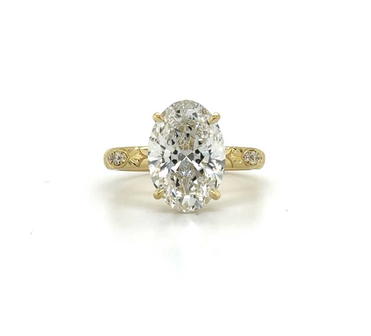 Top-down view of a 3 carat oval lab grown diamond engagement ring set in yellow gold with engraved side accents.