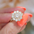 Close-up detail view of a 1.5 carat round lab diamond floral halo ring held between fingers highlighting the milgrain accent band.
