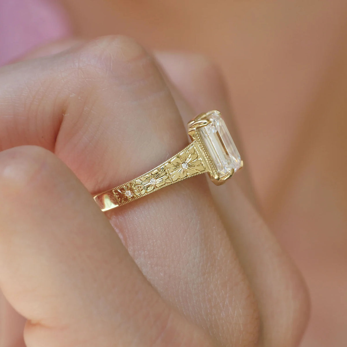 Side profile view on finger of a yellow gold 3 CT emerald cut lab diamond ring showing the basket height and floral band carving.