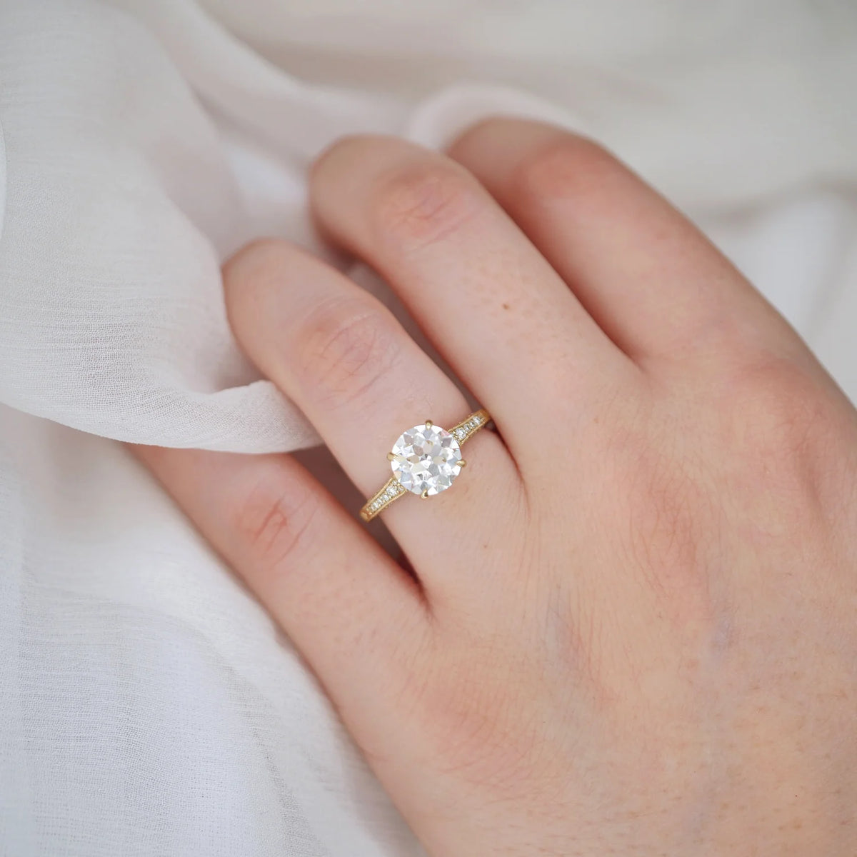Top view on hand of a 2 CT round lab grown diamond engagement ring set in 14K yellow gold with milgrain band details.