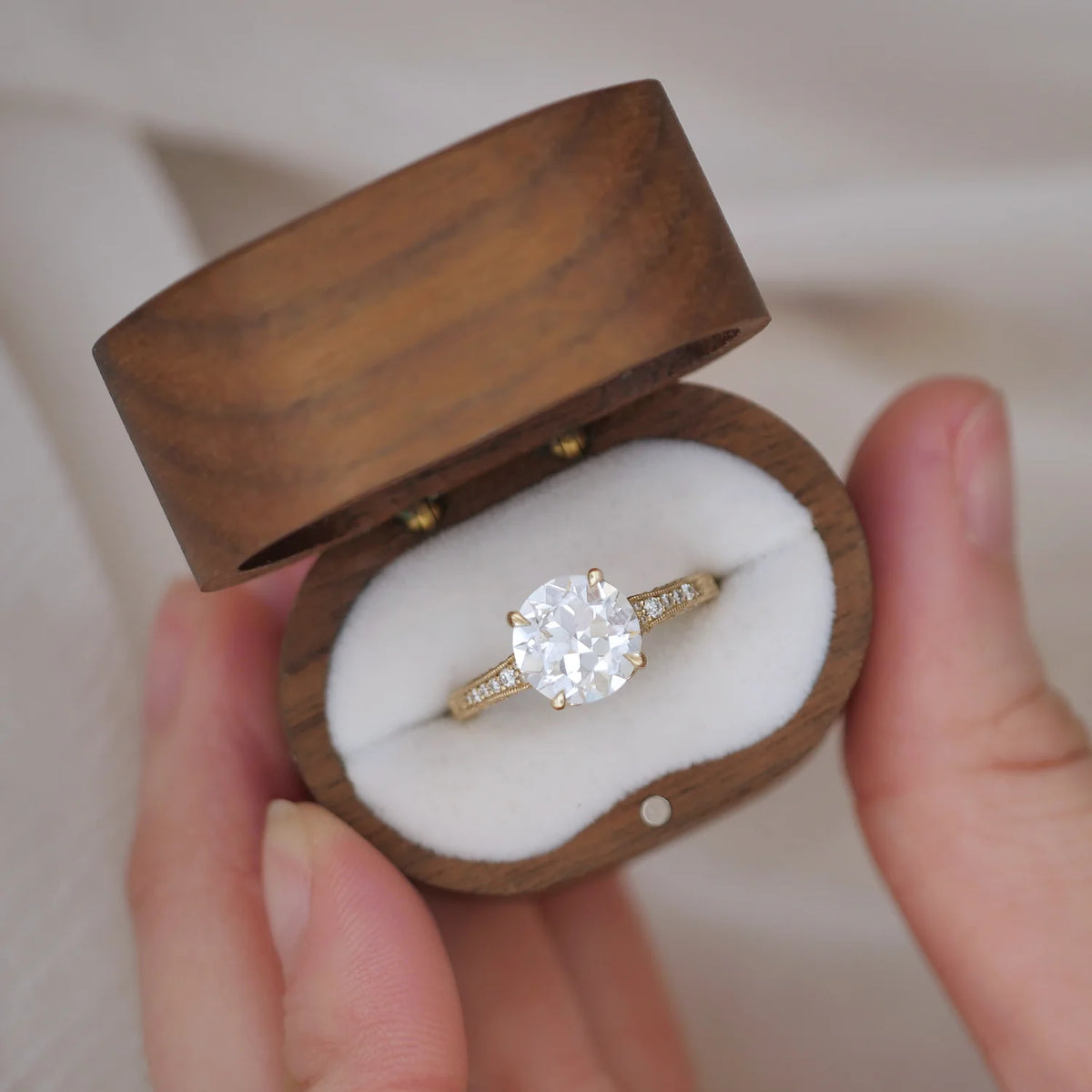 Top-down view of a 2 carat round lab grown diamond ring presented inside a dark wooden ring box.