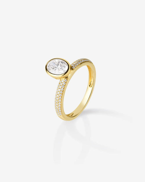 Angled view of a yellow gold 1.5 carat oval lab created diamond ring showing the sleek profile of the bezel setting and sparkling pavé accent band.