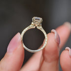 Close-up side profile of a 3 CT emerald cut lab grown diamond ring showing the hand-engraved floral basket setting and carved gold band held between fingers.