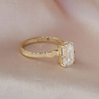 Angled view of a 3 CT emerald cut lab created diamond solitaire ring with hand-carved floral patterns on yellow gold.