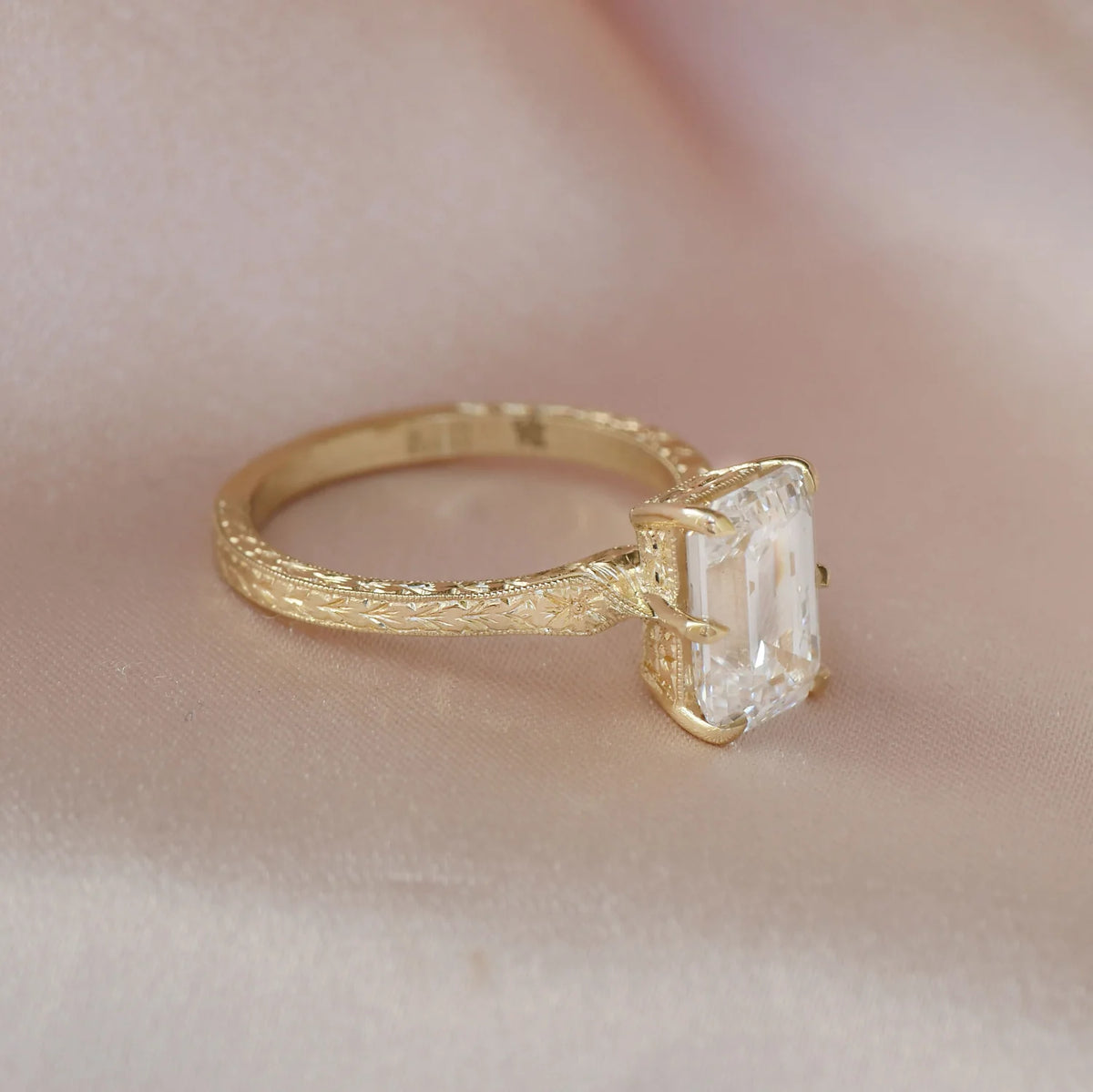 Angled view of a 3 CT emerald cut lab created diamond solitaire ring with hand-carved floral patterns on yellow gold.