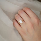 On-hand photo showing a 3 CT emerald cut lab grown diamond vintage engraved solitaire ring worn on finger over fabric.