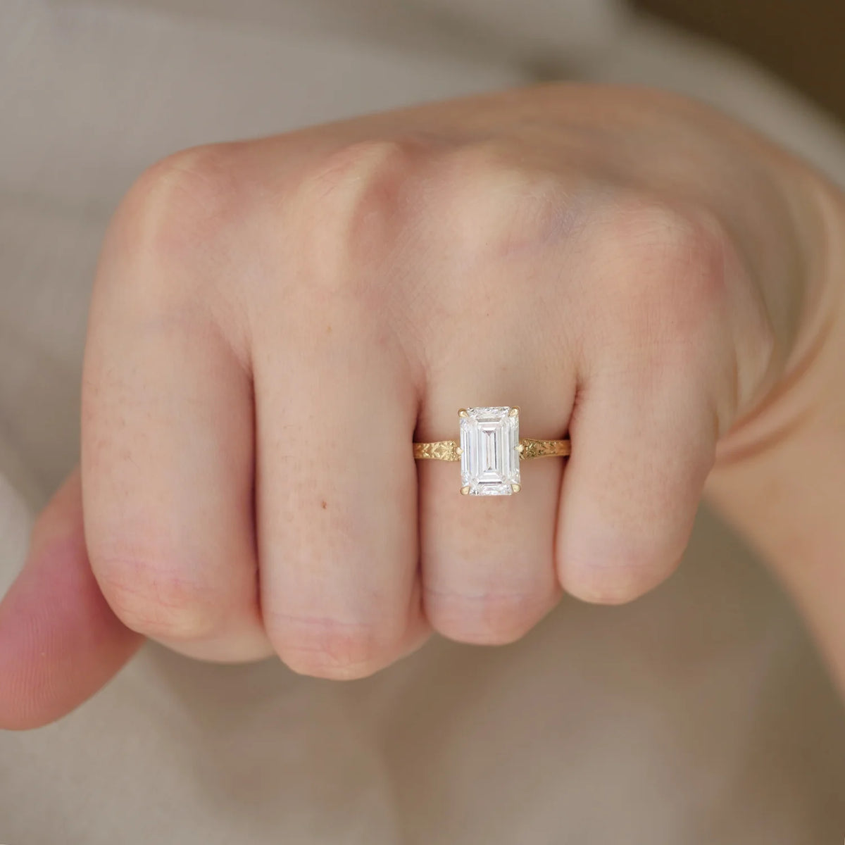 Direct view of a 3 CT emerald cut lab diamond ring with a vintage engraved gold band worn on a hand.