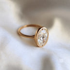 Angled side perspective of a 3 carat oval lab grown diamond engagement ring with a milgrain bezel setting in yellow gold.