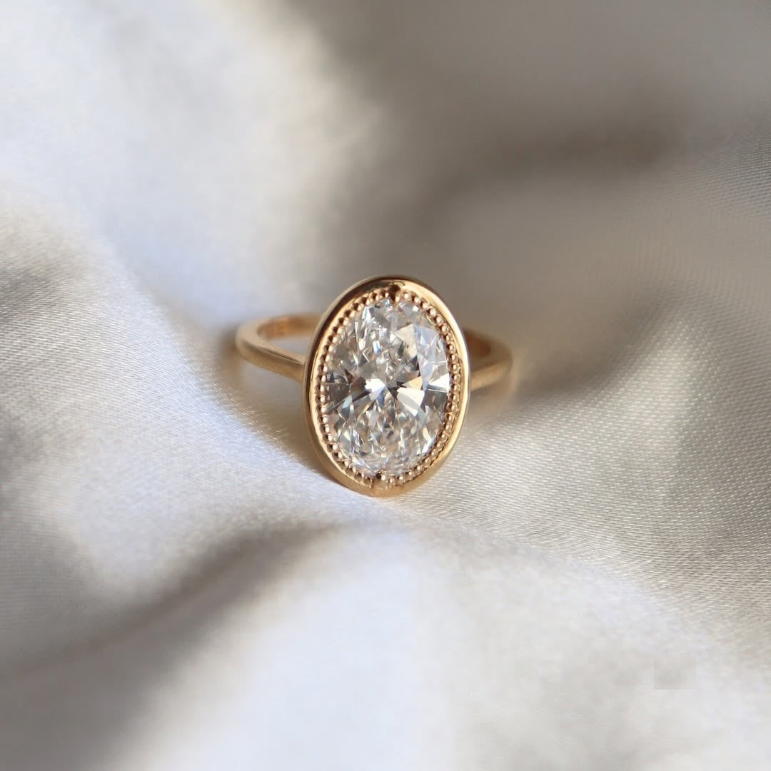 Top-down view showing a 3ct oval lab diamond encased in a detailed beaded milgrain bezel on a simple yellow gold band.