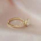 Side profile shot of a yellow gold 2 CT oval diamond ring with ornate under-gallery resting on silk.