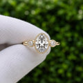 Top-down view of a 3 CT oval lab grown diamond three stone engagement ring with milgrain bezel borders and pear side diamonds in yellow gold.