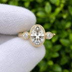 Close-up view of 3 carat oval lab created diamond ring with pear cut side stones and fine milgrain edging.
