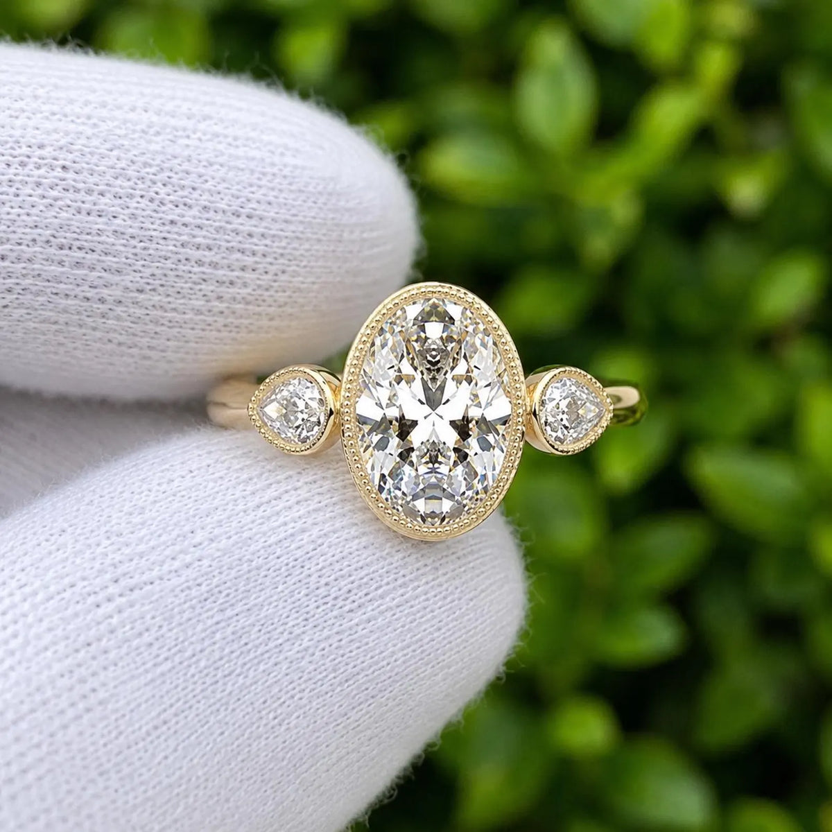 Close-up view of 3 carat oval lab created diamond ring with pear cut side stones and fine milgrain edging.