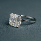 Angled view of a 3 CT Asscher cut lab grown diamond engagement ring with a micro-pavé hidden halo setting on a gray textured background.