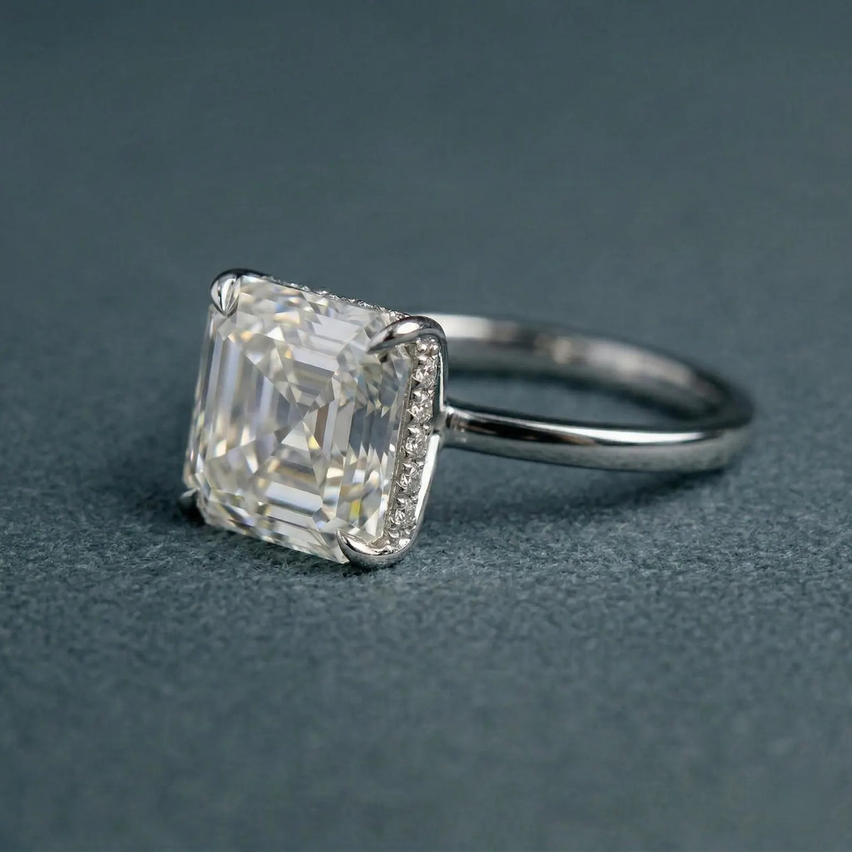 Angled view of a 3 CT Asscher cut lab grown diamond engagement ring with a micro-pavé hidden halo setting on a gray textured background.