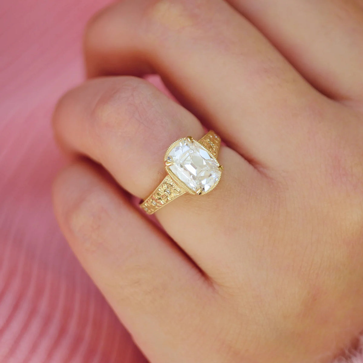 On-hand view of a 3 CT elongated cushion cut lab grown diamond engagement ring in yellow gold featuring vintage floral engraving.