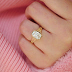 Close-up of a 3 carat cushion cut lab diamond ring with milgrain bezel and floral engraved shank worn on a finger.