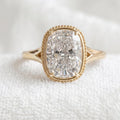 Top-down view of a 3 CT elongated cushion cut lab grown diamond engagement ring with a beaded milgrain bezel on white fabric.
