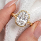 Close-up of a 3 CT elongated cushion lab diamond ring held between fingers displaying the beaded border and clear facets.