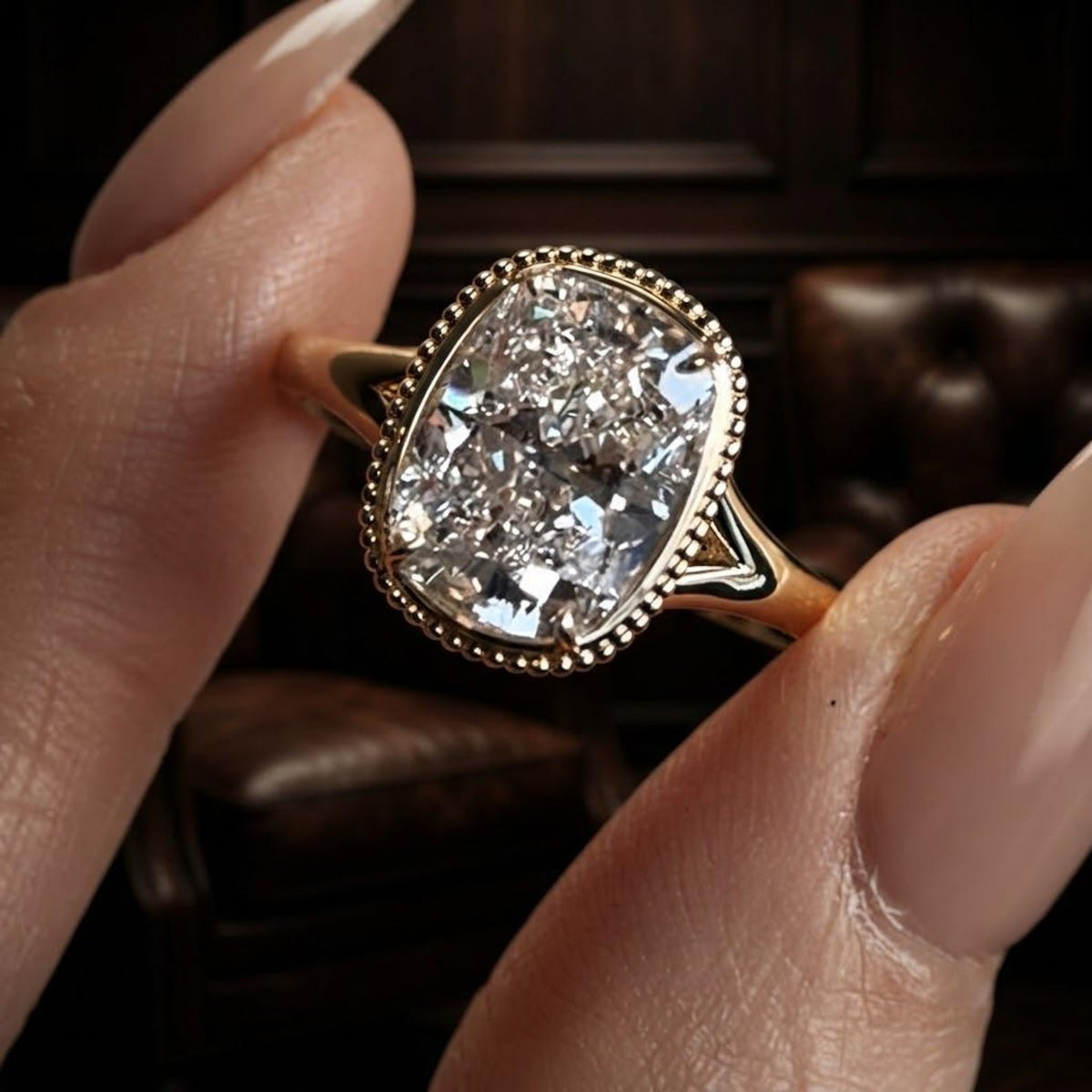 Macro view of a 3 carat elongated cushion cut lab grown diamond in a 14k yellow gold beaded bezel setting.