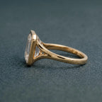 Angled side elevation of an emerald cut lab created diamond engagement ring showing the open cathedral bezel profile.