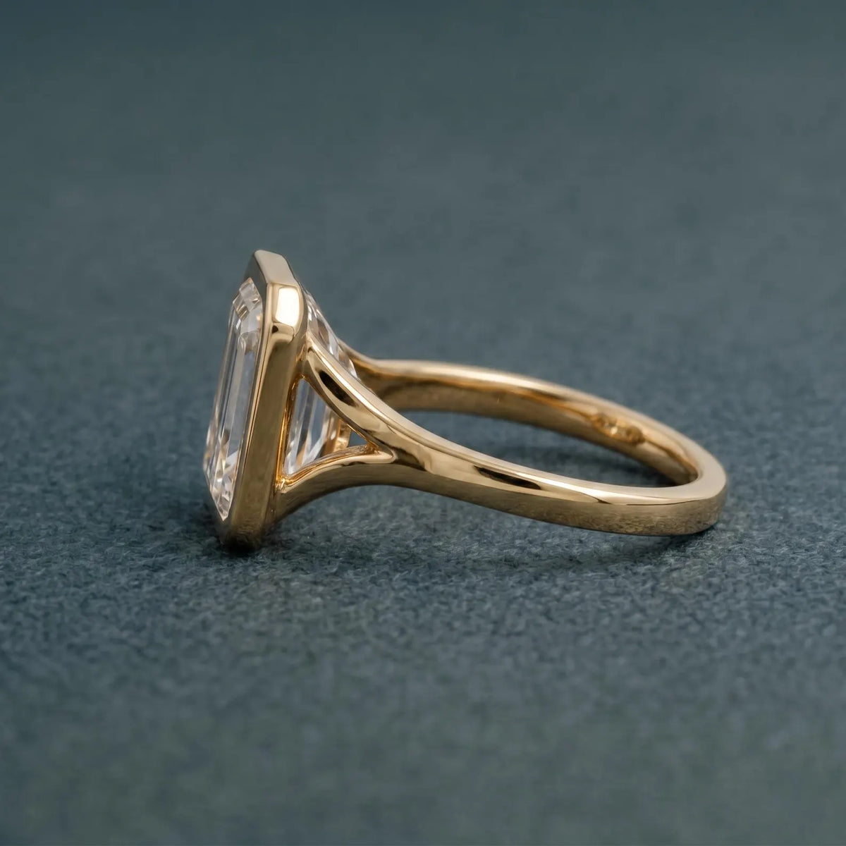 Angled side elevation of an emerald cut lab created diamond engagement ring showing the open cathedral bezel profile.